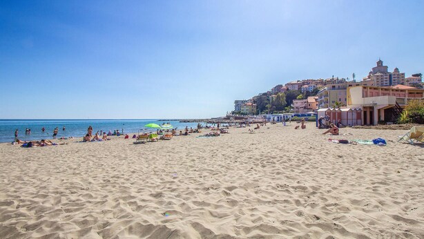 A beach with people sunbathing and swimming, buildings in the background, and a clear sky. - Beautiful home in Diano Calderina (Diano Calderina)