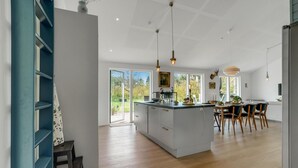 Eine moderne Küche mit Kochinsel, großen Fenstern und einer Essecke mit Holzkästen.
