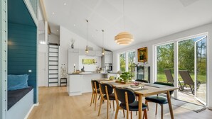 Eine moderne Küche mit weißen Schränken, ein Essbereich mit Holzkohle und eine große Glasschiebetür, die auf eine Terrasse im Freien führt.