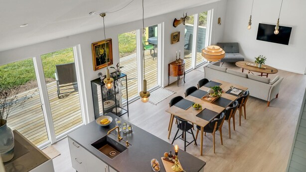 Eine großzügige Küche mit einer großen Kochinsel, ein Essbereich mit Holztisch und -stühlen sowie eine gemütliche Sitzecke mit einer Couch und Sesseln.