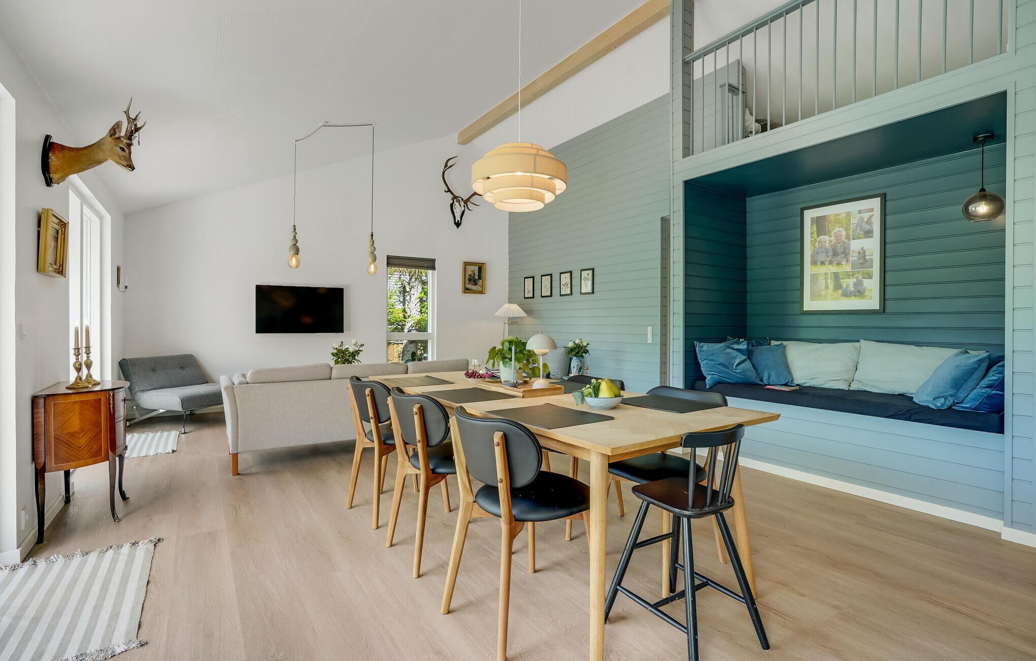 A modern dining area with a wooden table and chairs, a sofa, and a television mounted on the wall.