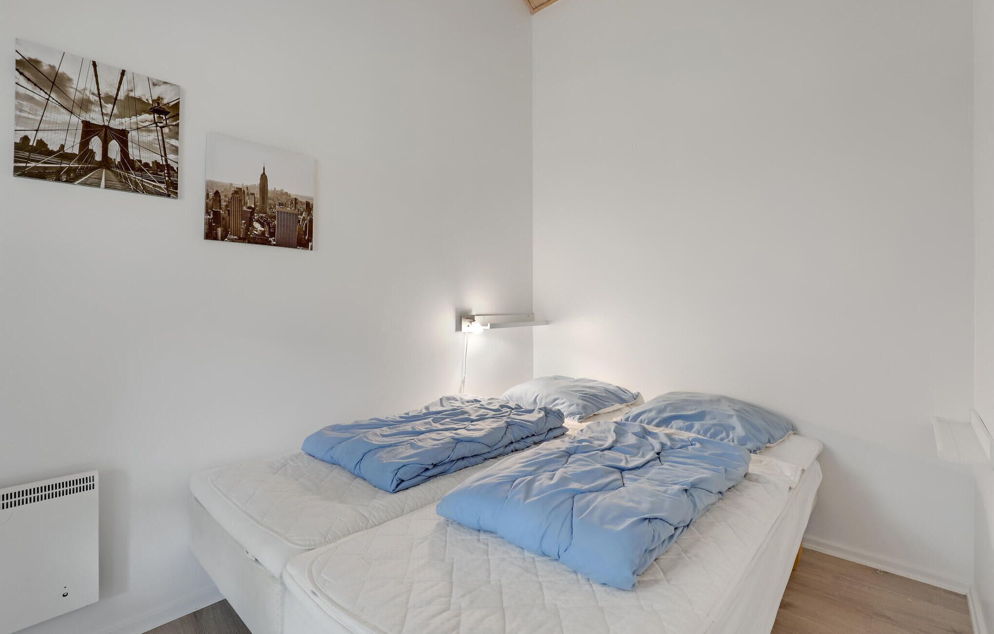 A bedroom with a bed, a wall-mounted light, and two framed pictures.