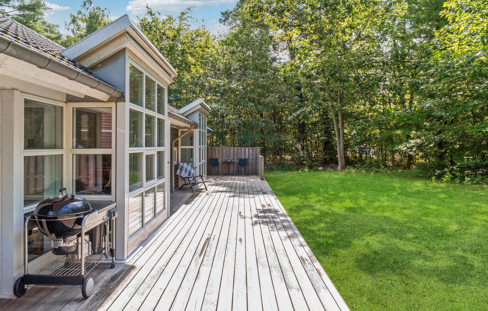 A deck with a grill and chairs, surrounded by a well-maintained lawn and trees.