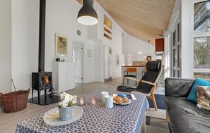 Relax in this spacious living area with a sofa near large windows offering a view of the outdoors, a dining table, and a wood-burning stove.