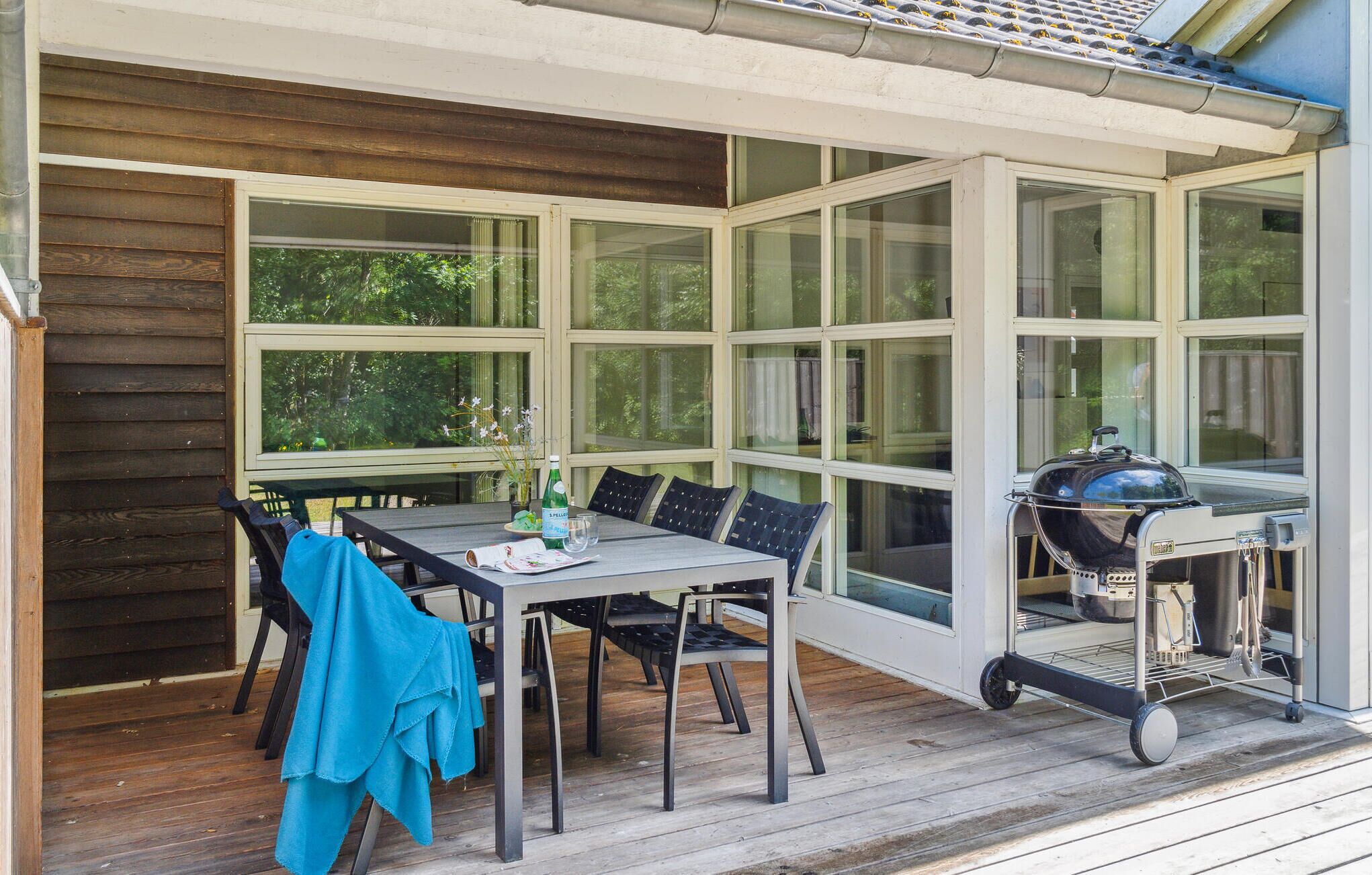 An outdoor patio with a table and chairs, a grill, and a covered area with large windows.