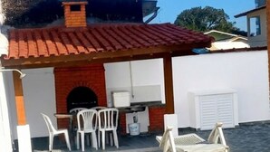 Una piscina con cubierta de piedra, un espacio de estar al aire libre techado con sillas y una estructura de ladrillo con chimenea.