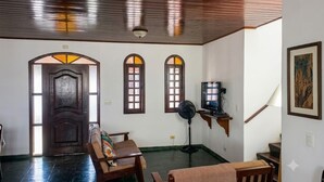 Una habitación con techo de madera, una puerta con paneles de vidrio, un televisor sobre un pedestal, un ventilador y una escalera.