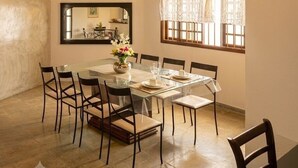 Un comedor con una mesa de vidrio, sillas, un jarrón de flores, un espejo y una ventana con cortinas.