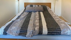 Una cama con una colcha acolchada con diversos diseños y una sola almohada.