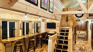 Interior de madeira com área de bar, banquetes, televisão e escada.