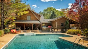 A wooden cabin with a swimming pool, outdoor seating, and a barbecue area.