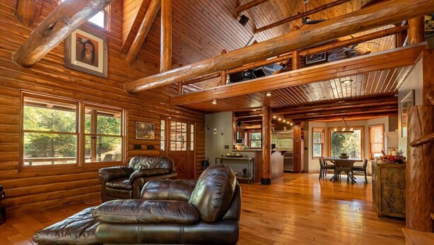 A spacious log cabin interior with a leather sofa, dining table, and kitchen area.