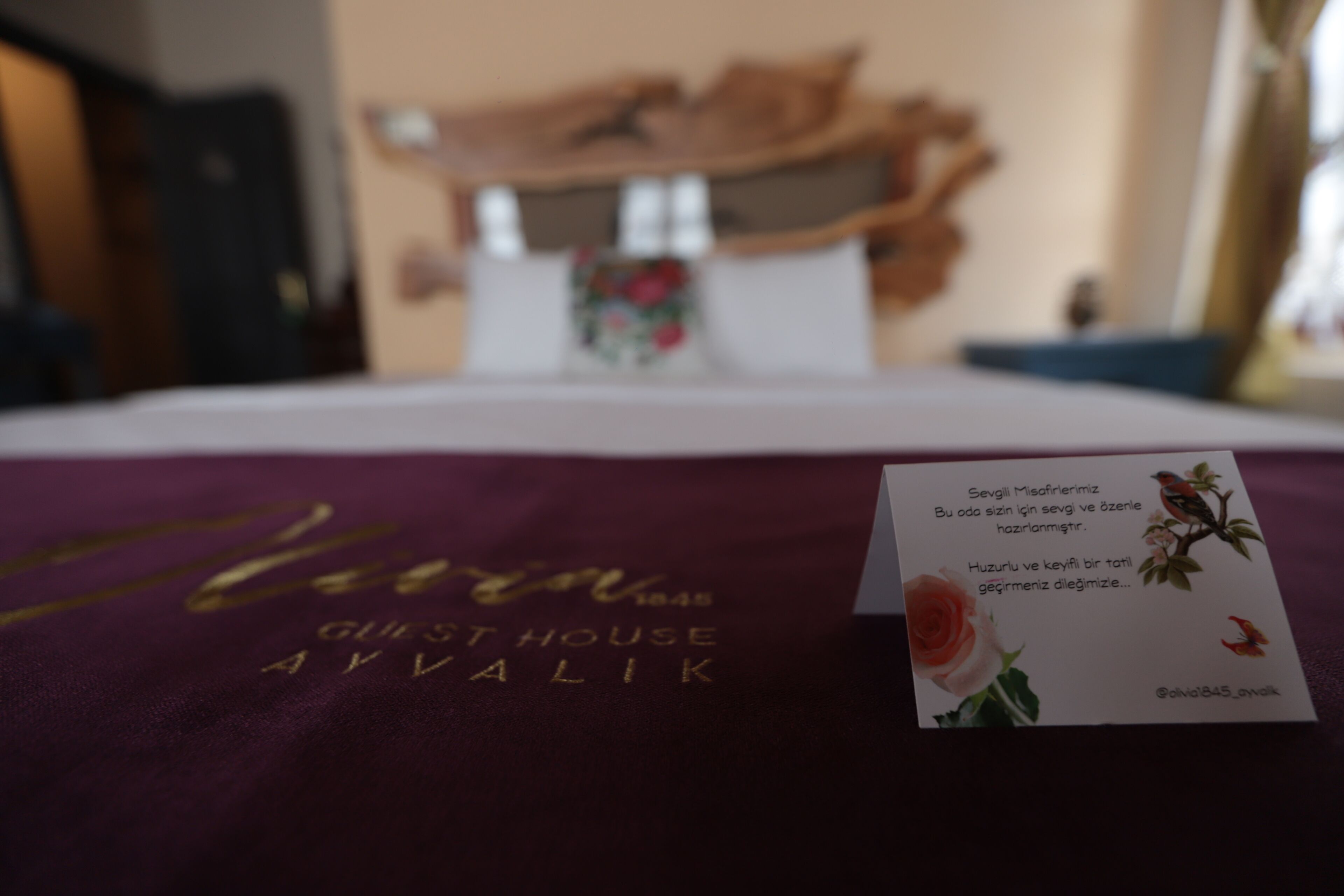 Hotellihuoneen sänky, jossa on violetti peitto ja sängyllä kortti.