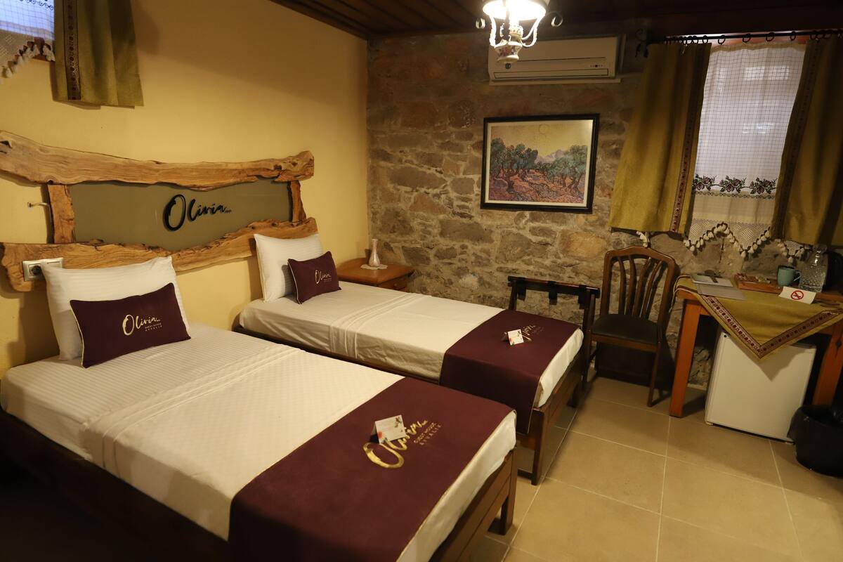 Een hotelkamer met twee bedden, een bureau, een stoel, een kleine koelkast en een stenen muur.