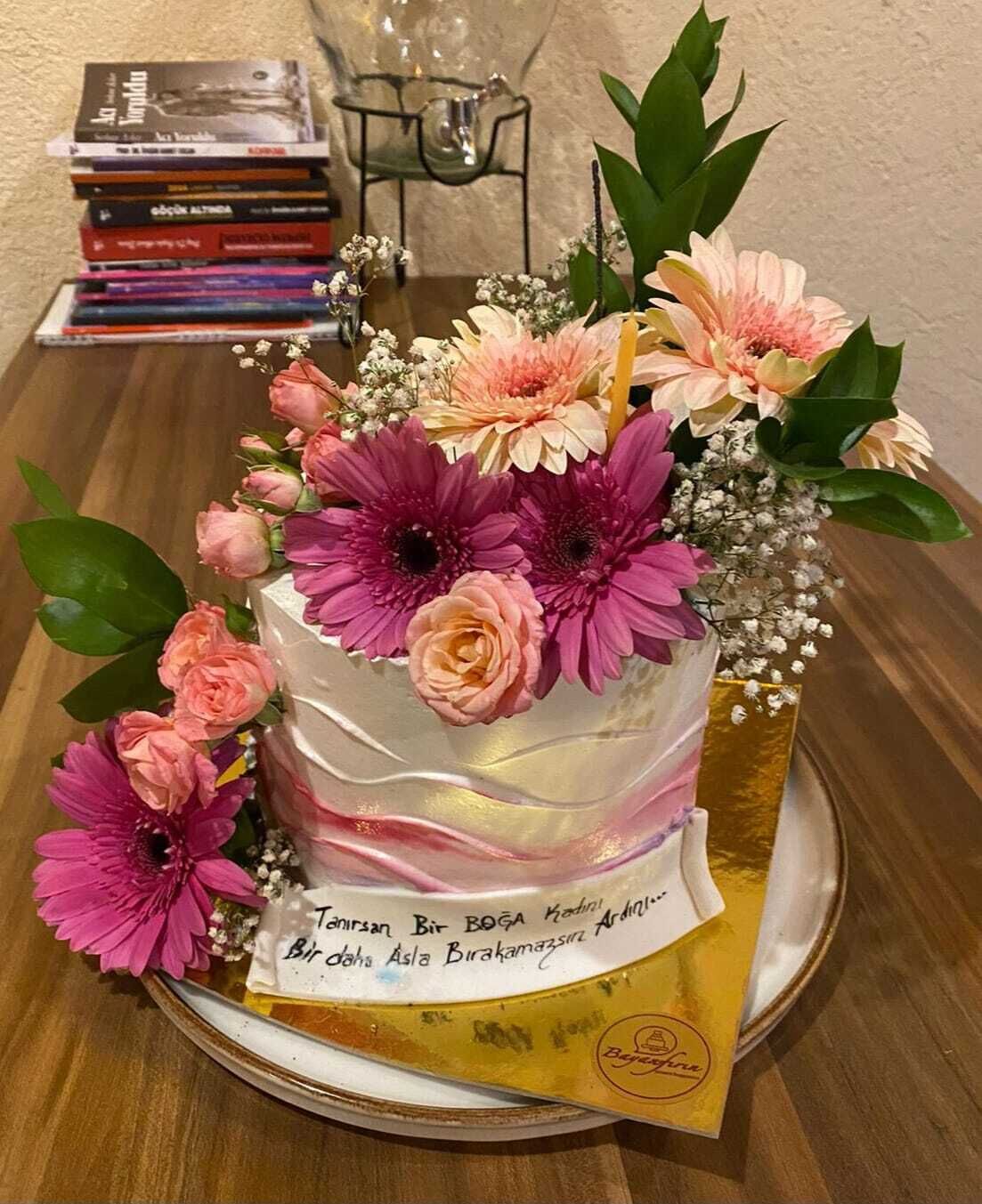 A cake with a message on a golden tray, surrounded by flowers on a table.