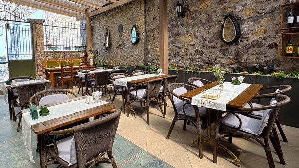 Un restaurant avec un mur en pierre, des tables en bois, des chaises en osier et un lustre.
