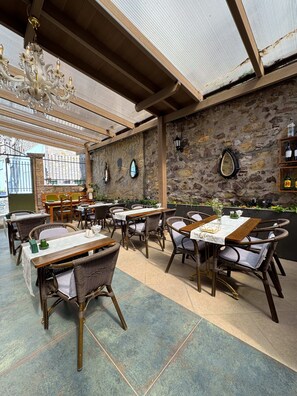 Ein Restaurant mit Steinwand, Holztischen, Korbstühlen und einer Chandelüster.
