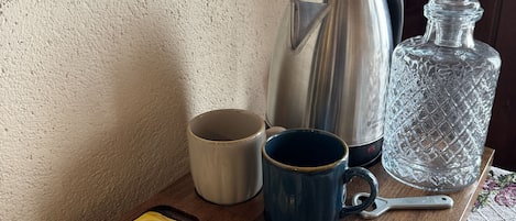 A wooden tray with coffee-making items including a Nescafe Classic coffee pod, Lipton Yellow Label tea sachets, Beyaz Seeker coffee pods, a blue mug, a stainless steel coffee pot, and a crystal decanter.