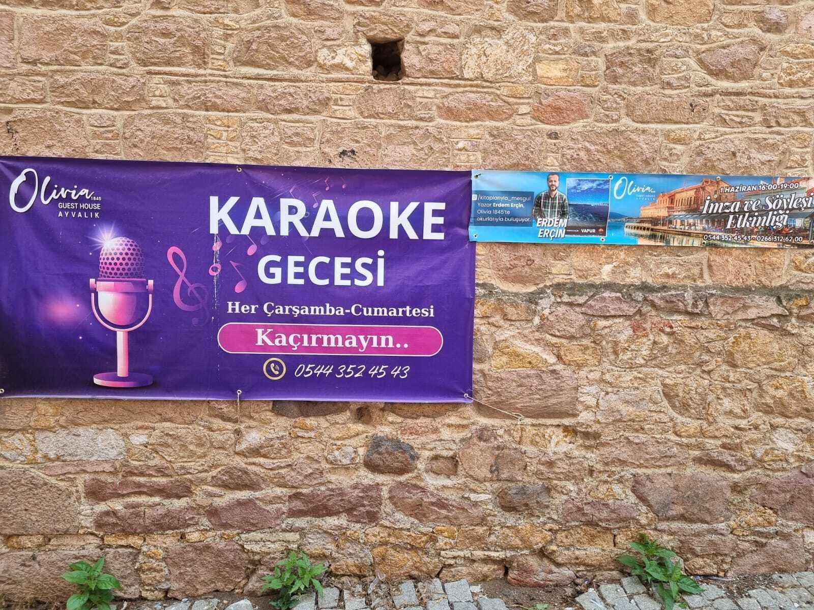Un cartel anunciando un evento de karaoke en una casa de huéspedes llamada Olivia, ubicada en Ayalık.