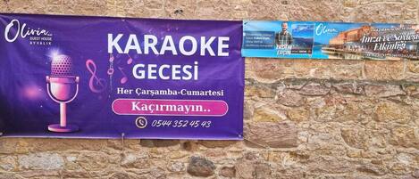 Un cartel anunciando un evento de karaoke en una casa de huéspedes llamada Olivia, ubicada en Ayalık.