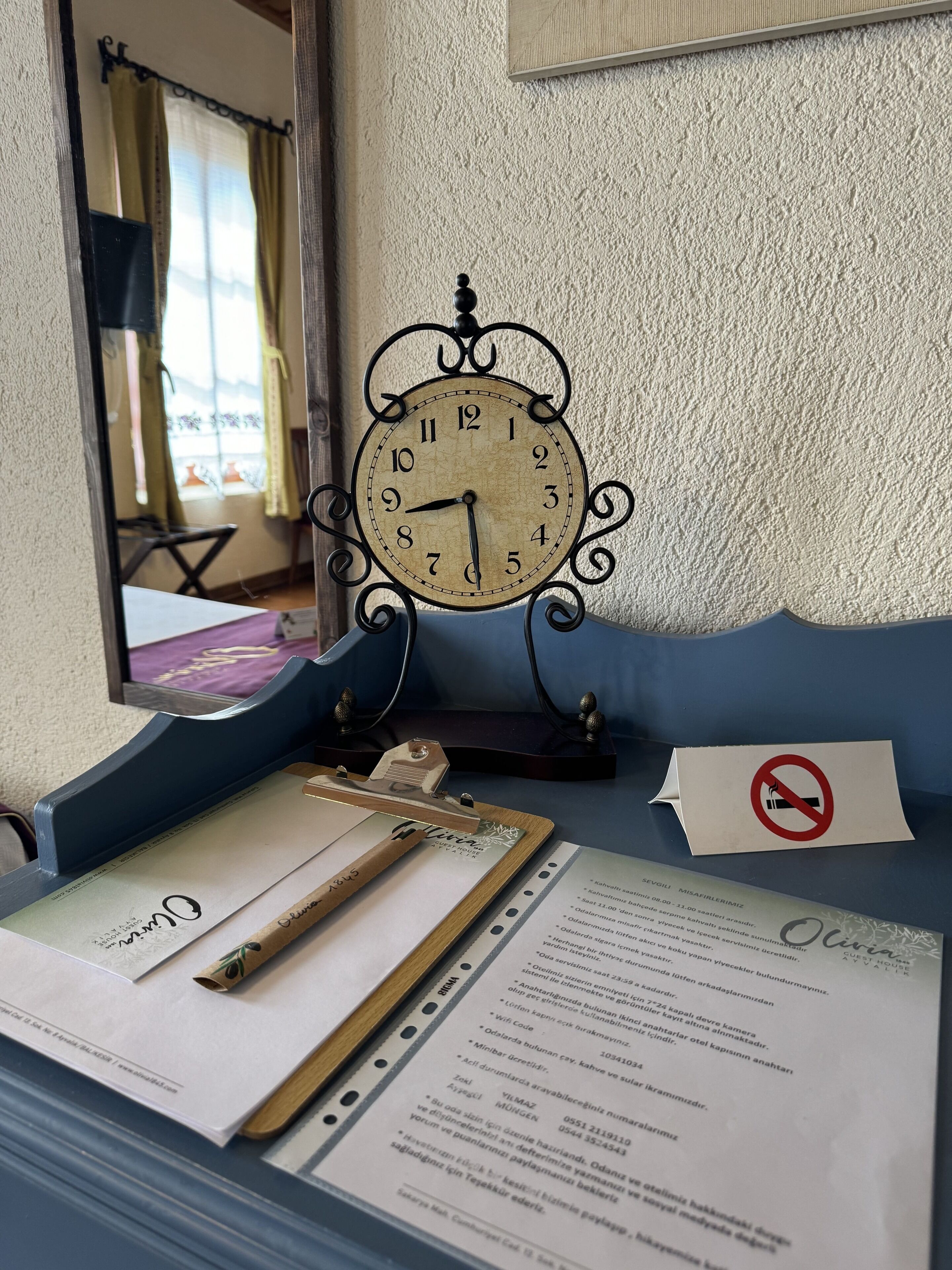 Una habitación con un reloj de pared de estilo vintage, un portapapeles con documentos y un cartel de prohibido fumar.