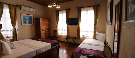 Une chambre avec deux lits, un plancher en bois, un bureau avec une chaise, une horloge et un téléviseur fixé au mur.