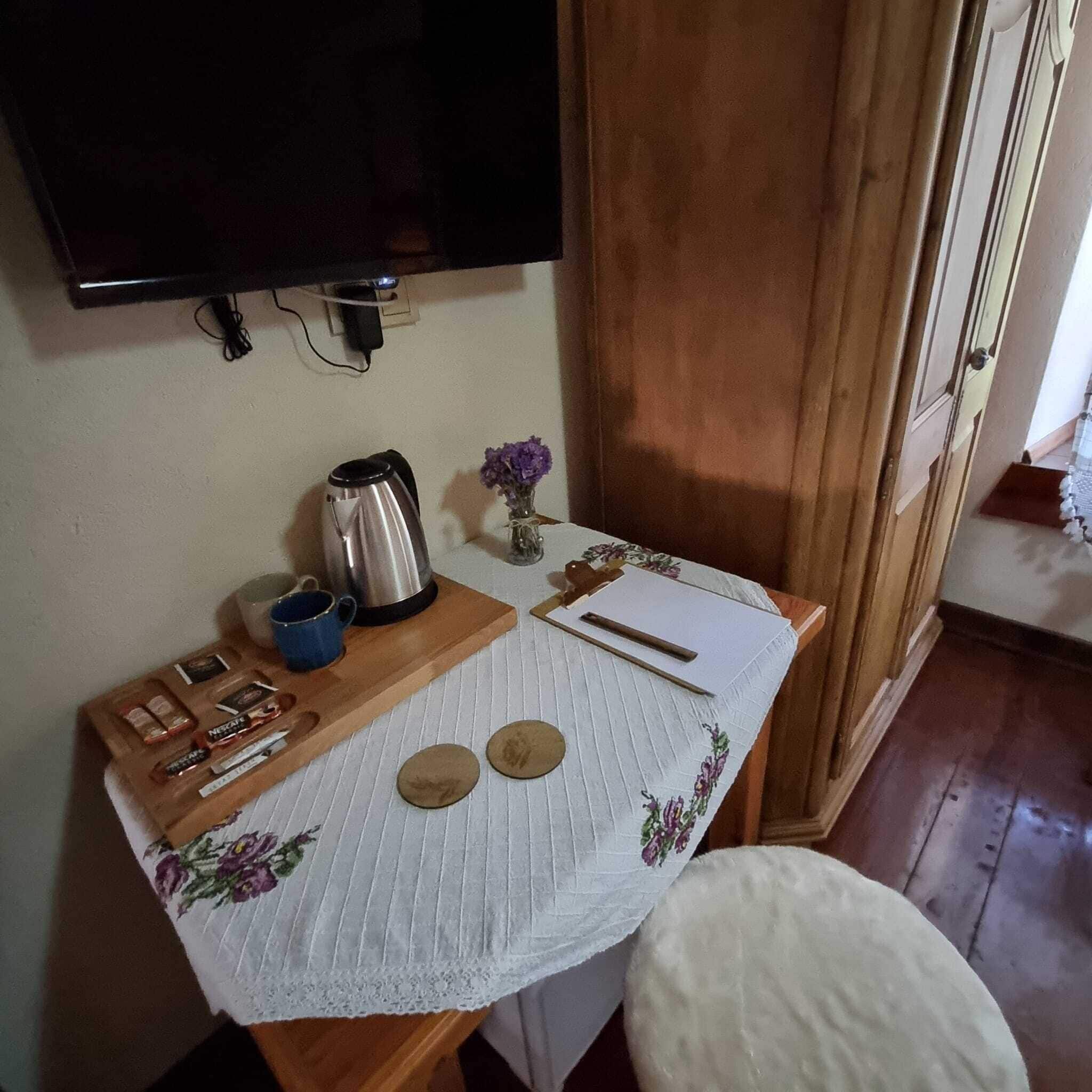 Une petite cuisine équipée d’une machine à café, d’une tasse, d’un plateau avec des en-cas, d’un vase avec des fleurs et d’une table avec un set de table.
