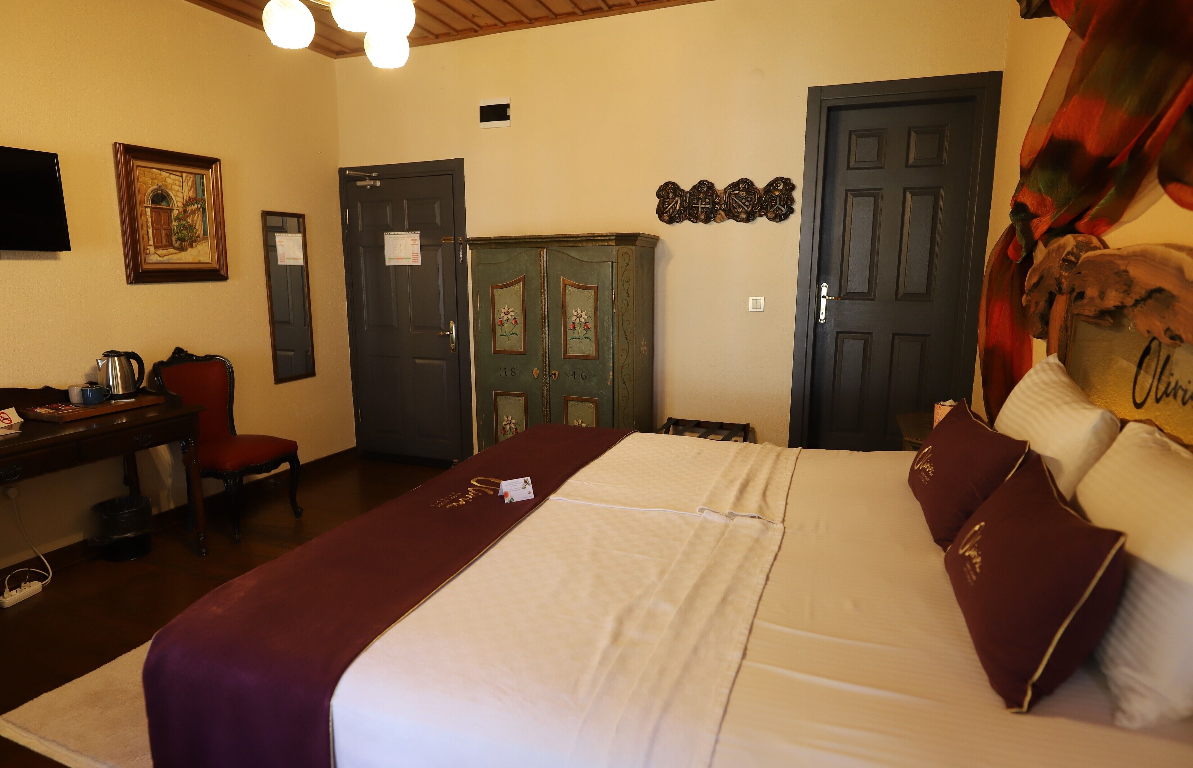 A hotel room with a large bed, a desk with a chair, a television, and a wardrobe.