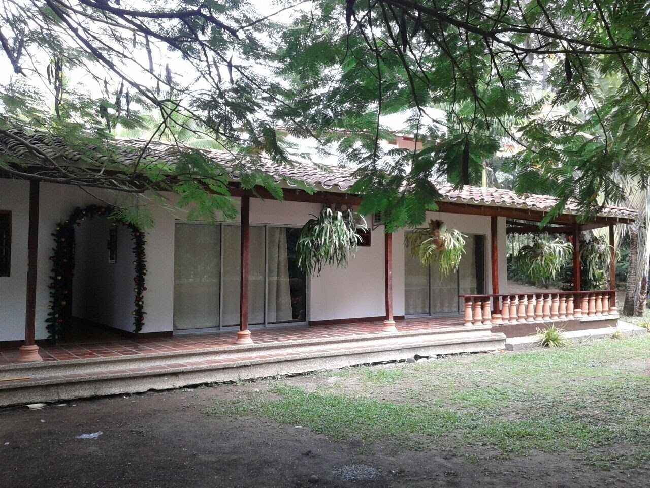 Un espacio al aire libre cubierto con techo de baldosas, baranda de madera y un pequeño jardín.