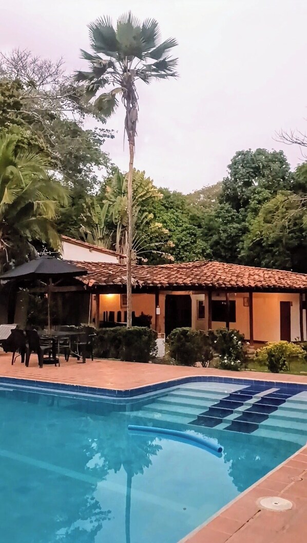 Una piscina con solárium de azulejos, una palmera y un edificio con tejado de cerámica.