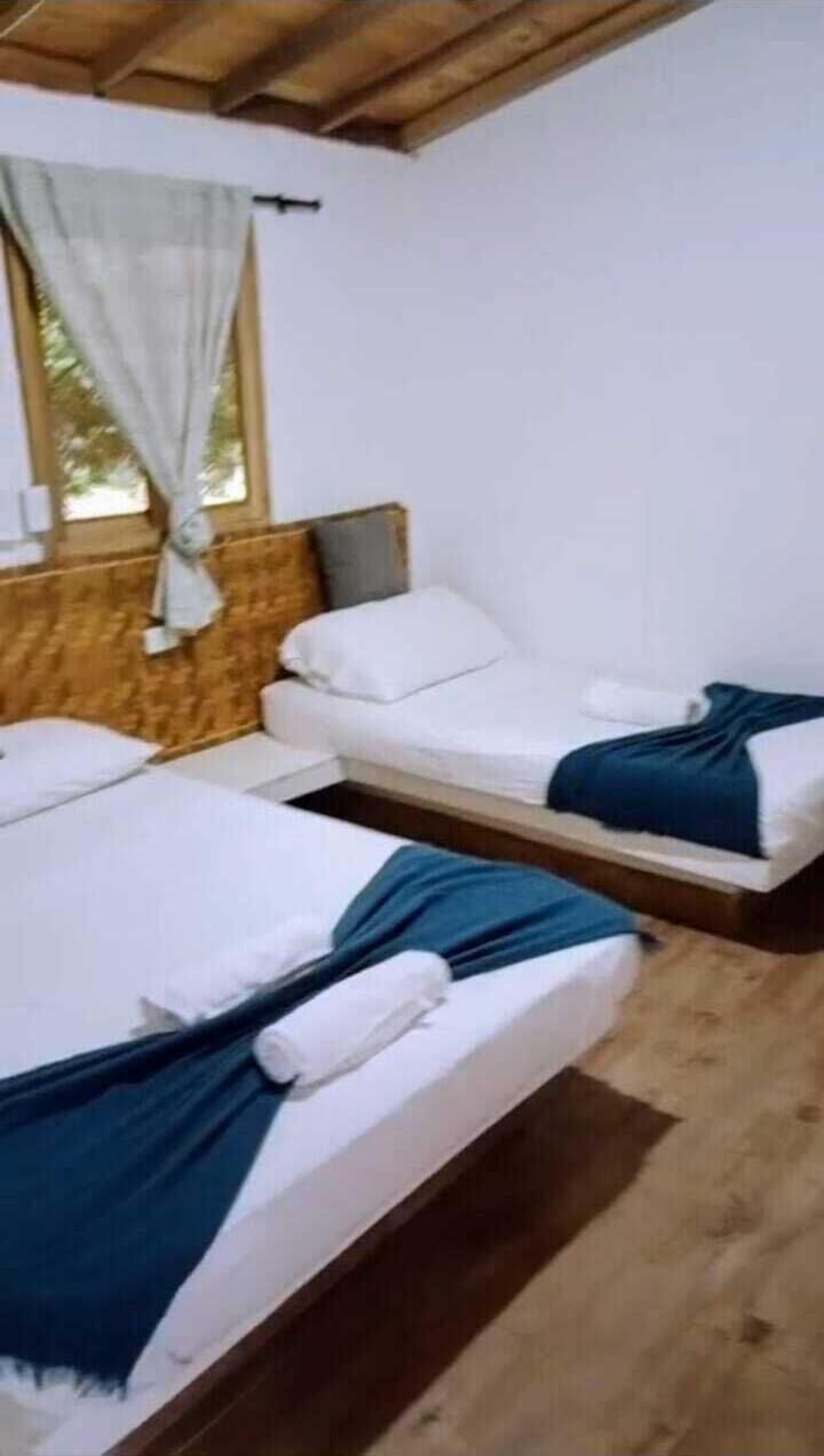 A room with two beds, wooden flooring, and a window with curtains.