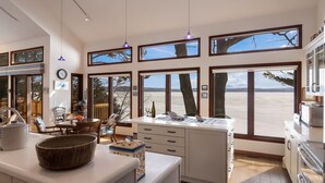 Cozinha moderna com grandes janelas, área de jantar e vista para a praia.