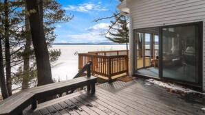 Um deck de madeira com um banco, uma porta de vidro que dá para o interior e vista para uma paisagem nevada.
