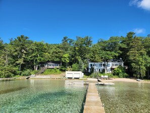 Una propietat al costat del port amb un moll de fusta que condueix a un llac cristal·lí, envoltada per un bosc dens i dues cases grans amb múltiples terrasses.