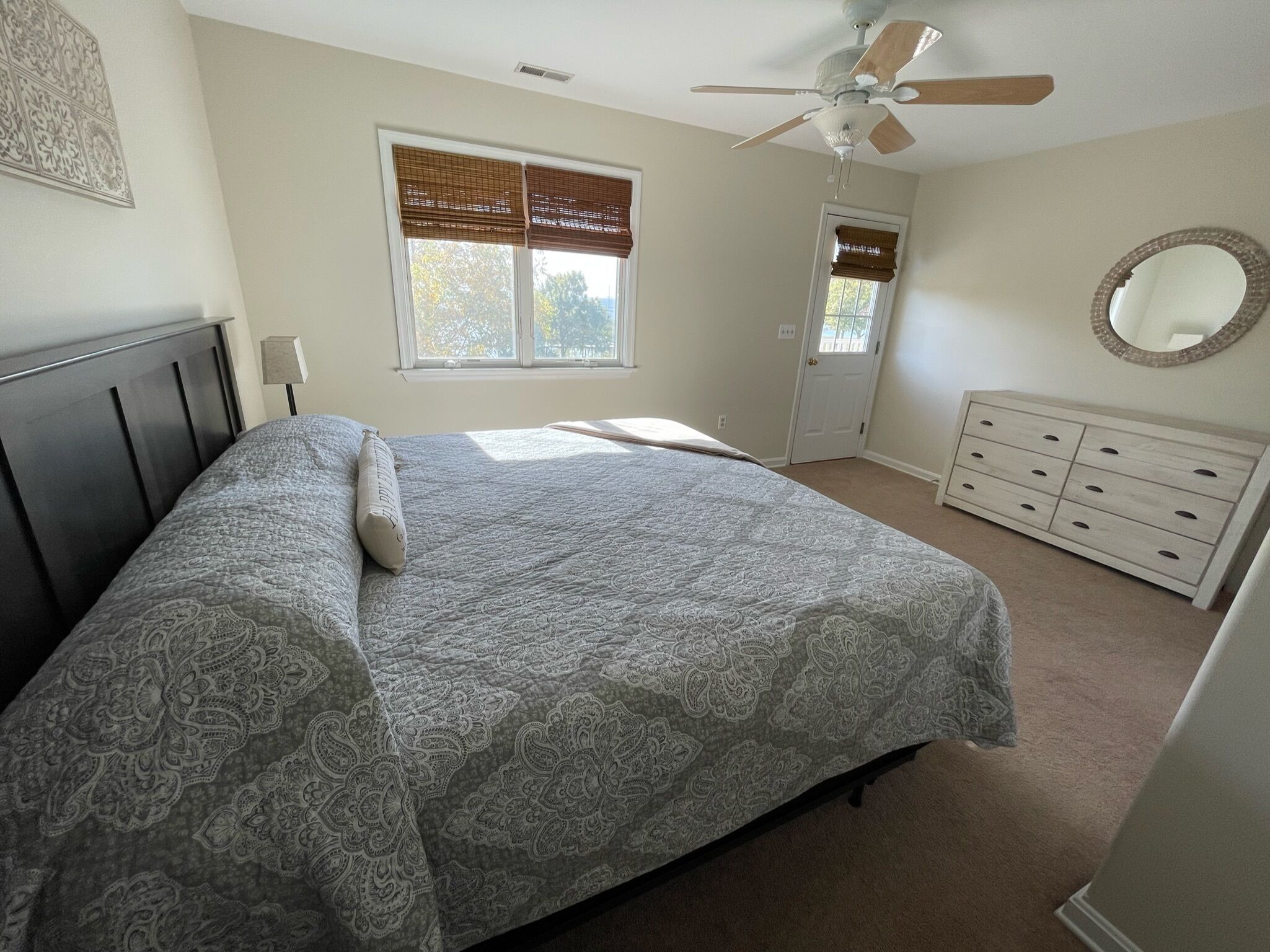 Ein Schlafzimmer mit Bett, Kommode, Deckenventilator und Fenster mit Jalousien.