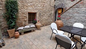 A stone-walled courtyard with a stone bench, a table with chairs, and potted plants.
