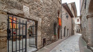 A narrow cobblestone street flanked by historic stone buildings with arched windows and a black metal gate.