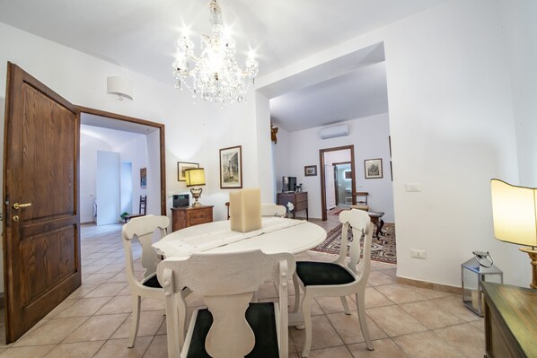 A dining area with a round table, white chairs, a chandelier, and a wooden door. - Saint François Apartment (Assisi)