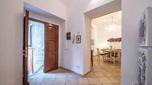 A hallway with a wooden door leading to a stone wall, a dining area with a chandelier, and a white cabinet with decorative patterns.