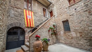 A narrow stone building with a flag, a black door, and steps leading to a balcony.