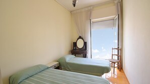 Une chambre avec deux lits, une petite table avec un miroir et une chaise près d’une fenêtre donnant sur un beau paysage.