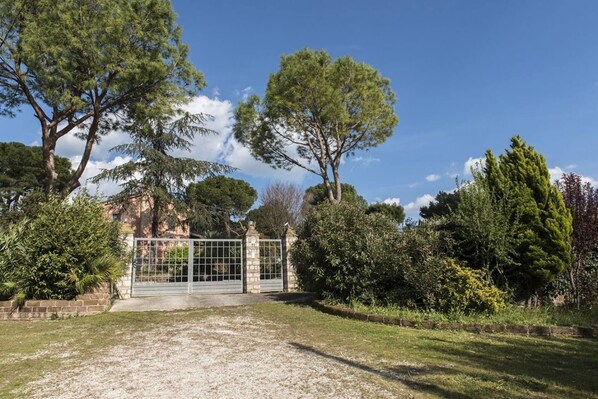 A gated property with a gravel driveway, surrounded by various trees and shrubs.