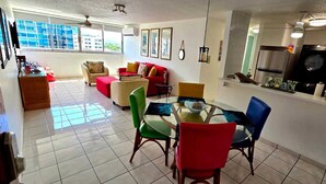 A living room with a red sofa, a glass dining table, and a kitchen area with a washing machine.