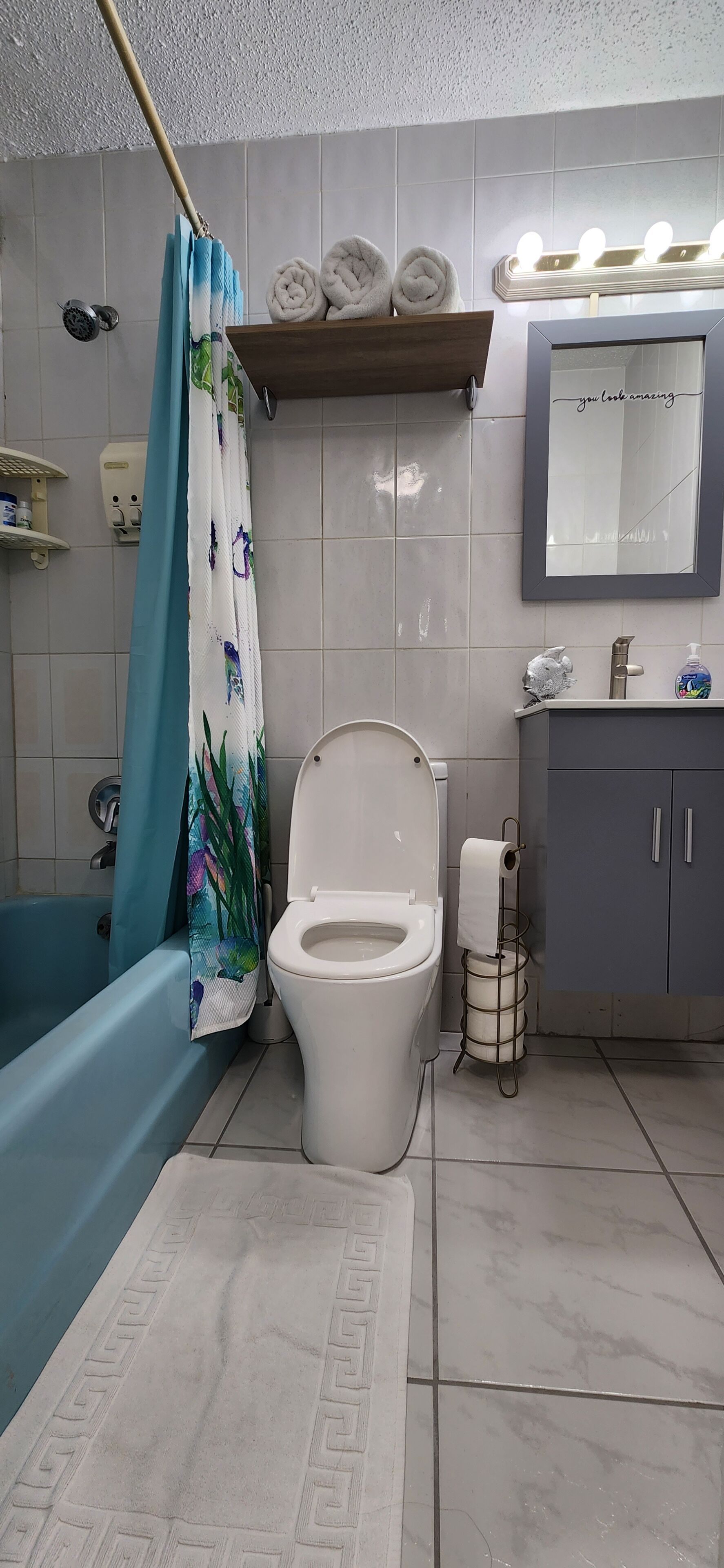Une salle de bain comprenant des toilettes, une baignoire, un rideau de douche, un meuble-lavabo avec un miroir et un porte-serviettes.