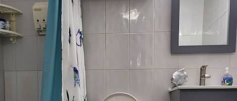 Une salle de bain comprenant des toilettes, une baignoire, un rideau de douche, un meuble-lavabo avec un miroir et un porte-serviettes.