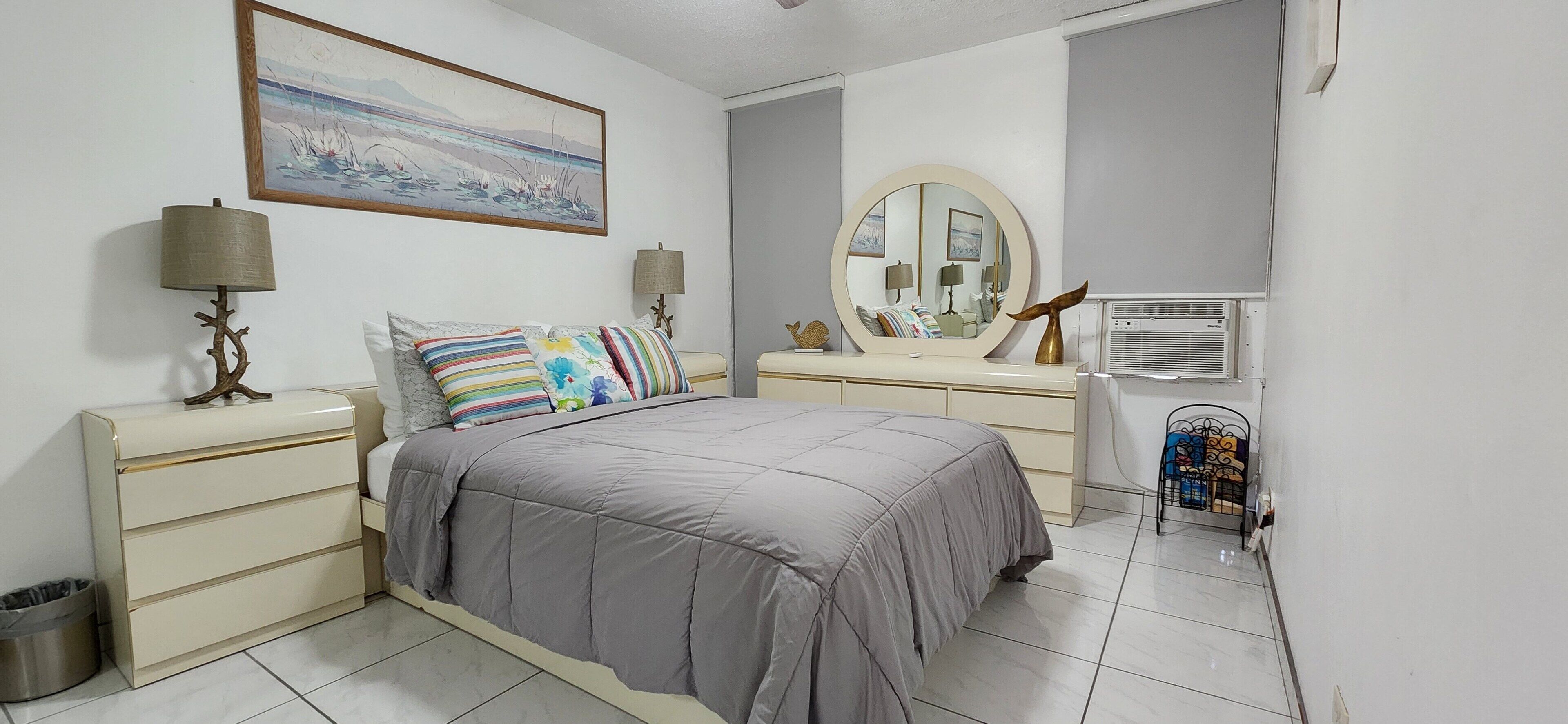 Un dormitorio con cama, mesitas de noche, cómoda, espejo y unidad de aire acondicionado.