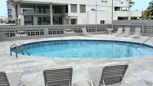 A swimming pool with lounge chairs and a tiled deck.