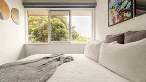 Quarto com uma janela grande, cama com roupa de cama branca e um cobertor de tricô.