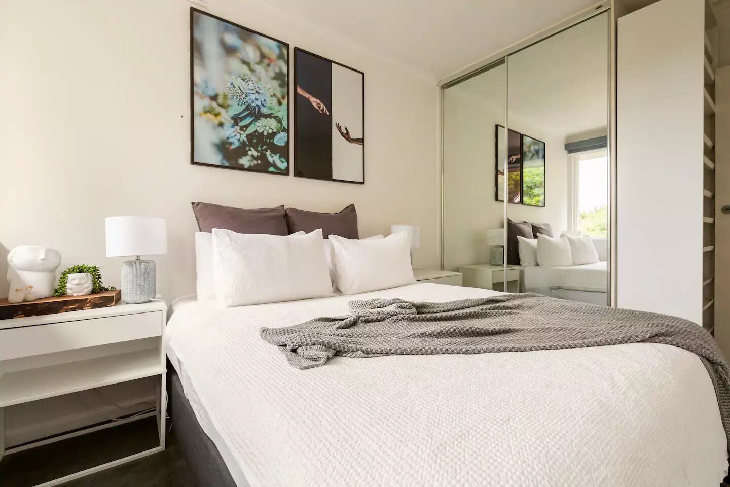 Un dormitorio moderno con una cama grande, ropa de cama blanca, una mesita de noche con una lámpara y un espejo.
