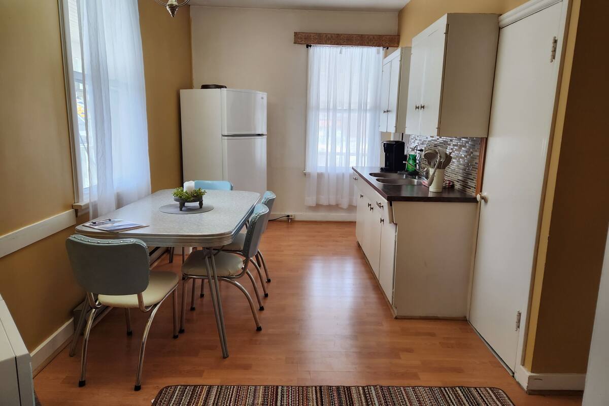 A compact kitchen with a dining table, chairs, a refrigerator, and a sink.